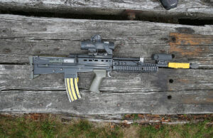 Assault rifle with scope and foregrip lying on weathered wooden planks.