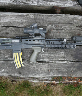 Assault rifle with scope and foregrip lying on weathered wooden planks.