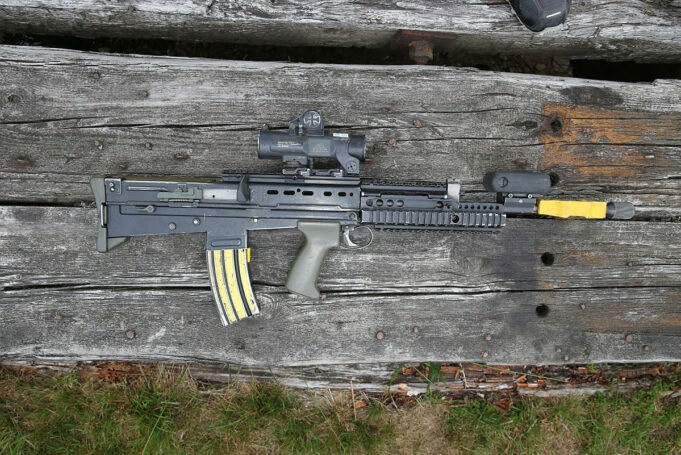 Machine guns among the military’s missing firearms Assault rifle with scope and foregrip lying on weathered wooden planks.