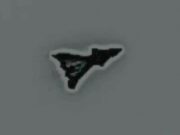 Small black irregular triangular sticker with a white outline on a gray surface, facing to the right.