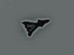 Small black irregular triangular sticker with a white outline on a gray surface, facing to the right.