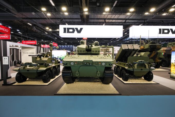 Military tanks on display at an exhibition hall with bright overhead lighting and large IDV signs in the background.