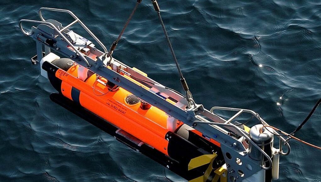 seafox Orange and gray underwater robotic device suspended above dark blue water, with a metal frame and yellow/black fins visible on the side.