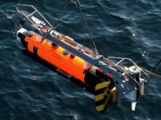 Support deal planned for Royal Navy mine disposal system Orange and gray underwater robotic device suspended above dark blue water, with a metal frame and yellow/black fins visible on the side.