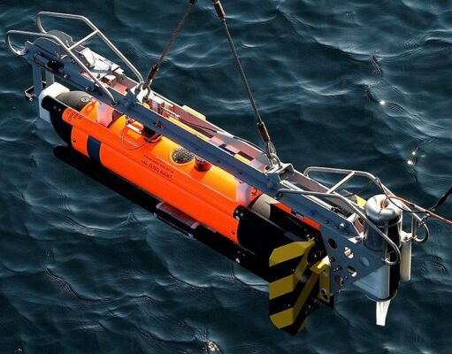 Orange and gray underwater robotic device suspended above dark blue water, with a metal frame and yellow/black fins visible on the side.