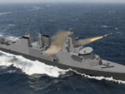 Grey naval warship at sea fires a missile from its launcher, with a helicopter on the aft deck and waves splashing nearby (hull number T31).