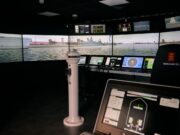 VR bridge simulator boosts Royal Navy training capacity Interior of a ship bridge simulator showing panoramic harbor screens and multiple navigation consoles.