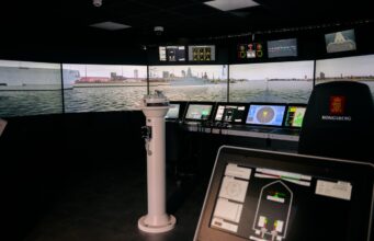 VR bridge simulator boosts Royal Navy training capacity Interior of a ship bridge simulator showing panoramic harbor screens and multiple navigation consoles.