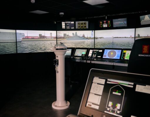 VR bridge simulator boosts Royal Navy training capacity Interior of a ship bridge simulator showing panoramic harbor screens and multiple navigation consoles.