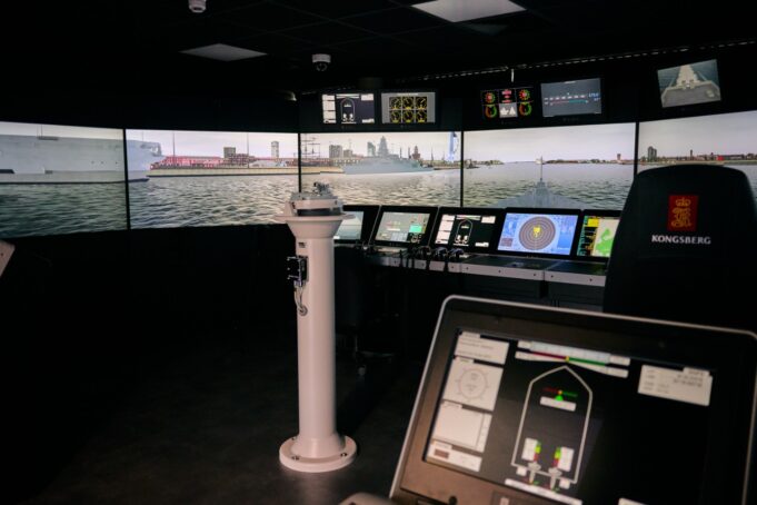 VR bridge simulator boosts Royal Navy training capacity Interior of a ship bridge simulator showing panoramic harbor screens and multiple navigation consoles.