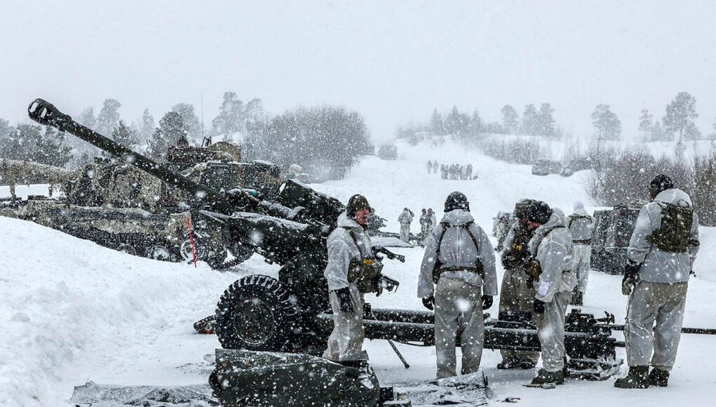 105 Soldiers in white winter gear stand around a large artillery cannon in a snowy battlefield, preparing or inspecting the weapon as snow falls heavily.
