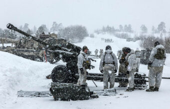 BAE lands £4M UK deal for artillery and gun components Soldiers in white winter gear stand around a large artillery cannon in a snowy battlefield, preparing or inspecting the weapon as snow falls heavily.