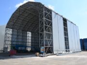 New building rises at Navantia’s Methil yard in Fife Construction site: a large steel-framed warehouse under a curved roof with white fabric walls against a blue sky.