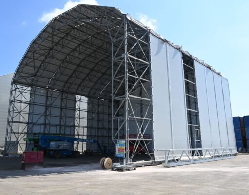 New building rises at Navantia’s Methil yard in Fife Construction site: a large steel-framed warehouse under a curved roof with white fabric walls against a blue sky.
