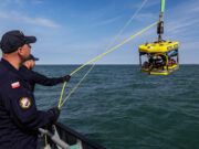 Sea Breeze brings allied EOD divers to Portland waters Polish naval personnel lower a yellow underwater drone (ROV) into the sea from a ship, secured by yellow cables against a blue sky and water.