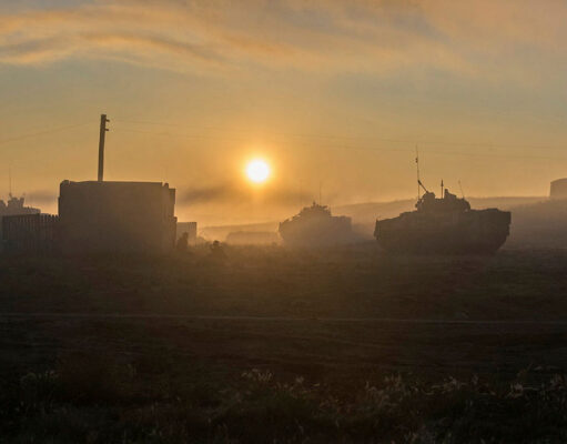 UK to expand drone testing across Canadian prairie base Sunrise over a foggy field with silhouettes of tanks and a small building in the distance.
