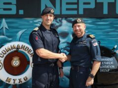 New commanding officer takes charge of mine warfare group Two Royal Navy officers shake hands in front of a blue maritime backdrop, smiling at the camera.