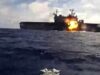 Naval warship at sea with a large explosion and fire on its side of the deck.