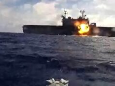 Naval warship at sea with a large explosion and fire on its side of the deck.