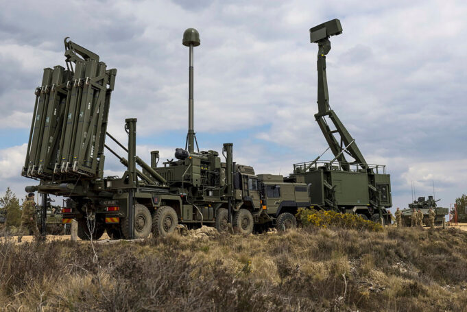 Military mobile missile system on a truck with multiple vertical launch tubes, in a dry open area under a cloudy sky.