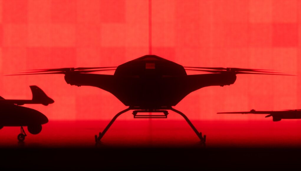 AR6_PRESS_05 Front-facing silhouette of a quadcopter drone with landing gear against a red background