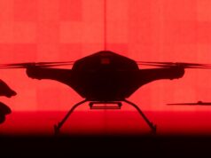 Tekever unveils AR6 drone able to lift 200kg over 500km Front-facing silhouette of a quadcopter drone with landing gear against a red background