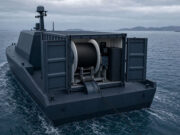 Autonomous-looking marine vessel with a large spool winch and deck equipment, sailing in open water.