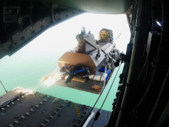 Royal Navy drone boat airdropped from A400M in world first View from inside an open cargo plane showing a secured pallet and gear near the rear ramp, with the turquoise sea visible below.