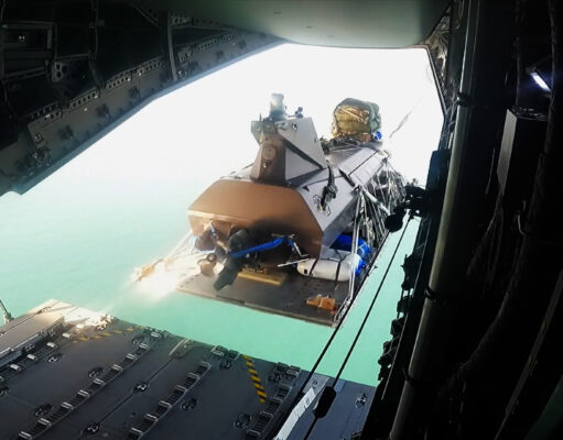 Royal Navy drone boat airdropped from A400M in world first View from inside an open cargo plane showing a secured pallet and gear near the rear ramp, with the turquoise sea visible below.