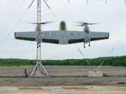 Sikorsky’s Nomad 100 drone completes first flight tests Three-rotor unmanned aircraft mounted on a test stand with supporting cables on a runway and a tree line in the background.