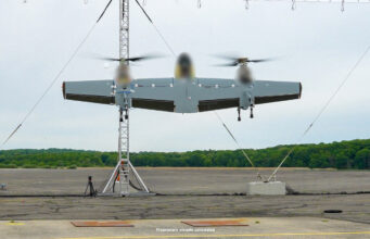 Sikorsky’s Nomad 100 drone completes first flight tests Three-rotor unmanned aircraft mounted on a test stand with supporting cables on a runway and a tree line in the background.