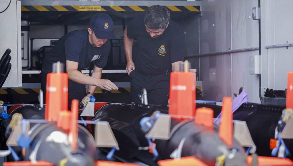 FLEET-20260702-XL0064-004 Two emergency responders in navy uniforms inspect equipment inside a transport vehicle, with orange safety posts in the foreground.