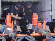 Minehunting teams embark warships ahead of global tasks Two emergency responders in navy uniforms inspect equipment inside a transport vehicle, with orange safety posts in the foreground.