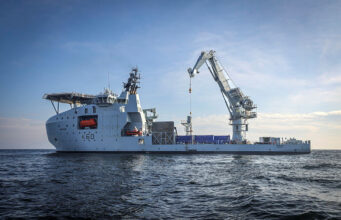 Britain’s seabed warfare vessel to get upgrades Large white offshore support vessel with a tall crane on calm blue sea, hull marked K60.