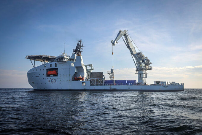Large white offshore support vessel with a tall crane on calm blue sea, hull marked K60.