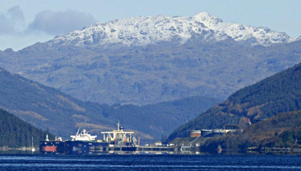 Finnart_oil_terminal_-_geograph.org.uk_-_6327240 Snowy mountains rise behind a harbor with ships moored along the quay, calm blue water in the foreground.
