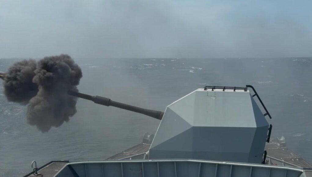HNHSE82WQAAlLb2 Military vessel at sea fires its main gun, ejecting a dense black smoke plume from the muzzle.