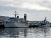 Royal Navy’s last Hunt-class minehunter to go by 2031 Two large grey military ships docked at a pier on a cloudy day, reflecting in calm water.