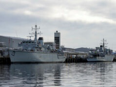Royal Navy’s last Hunt-class minehunter to go by 2031 Two large grey military ships docked at a pier on a cloudy day, reflecting in calm water.