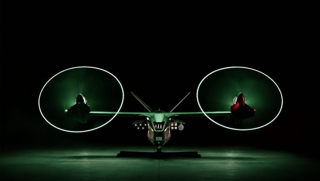 IMG-20260720-WA0000 Front view of a futuristic dual-rotor aircraft with two large glowing green circular rotors, parked in a dark hangar.