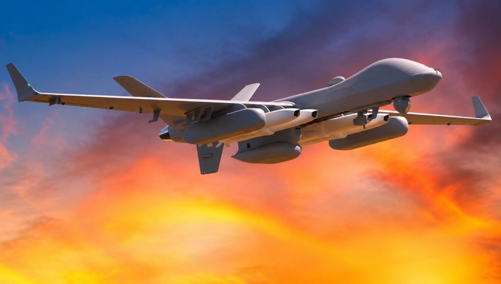 IMG-20260720-WA0003 Unmanned military drone in flight with an orange sunset sky behind it.