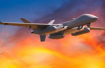 Stealth strike missile heading for MQ-9B drone family Unmanned military drone in flight with an orange sunset sky behind it.