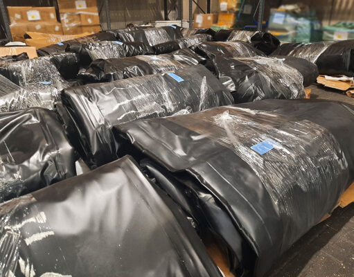 NCA seizes 25 smuggling boats and engines at Felixstowe Warehouse scene with large black plastic-wrapped bundles on pallets, stacked in aisles.