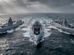 British shipyard gearing up to build drone warships Three modern gray warships sail in rough seas, creating white wake under a stormy, sun-slashed sky.