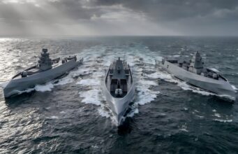 British shipyard gearing up to build drone warships Three modern gray warships sail in rough seas, creating white wake under a stormy, sun-slashed sky.