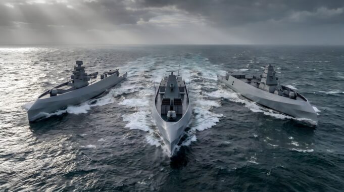 British shipyard gearing up to build drone warships Three modern gray warships sail in rough seas, creating white wake under a stormy, sun-slashed sky.