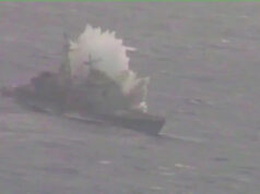 Small boat on rough water with a large white spray behind it, suggesting a splash or plume from the vessel.