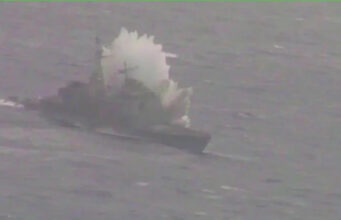 Small boat on rough water with a large white spray behind it, suggesting a splash or plume from the vessel.