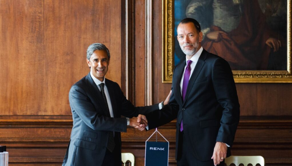 RENK_David_Brown_Defence Two businessmen in dark suits shake hands over a table in a wood-paneled room, with a RENK banner between them and nameplates in front of each person.