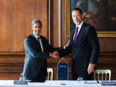 RENK to buy UK naval gearbox maker David Brown Defence Two businessmen in dark suits shake hands over a table in a wood-paneled room, with a RENK banner between them and nameplates in front of each person.